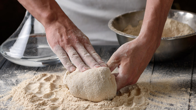 Hands pressing into dough on wooden surface