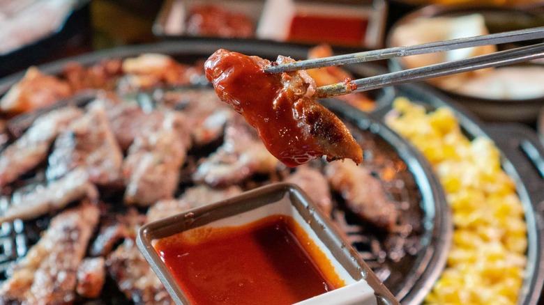 Chopsticks holding Korean barbecue pork and dipping sauce