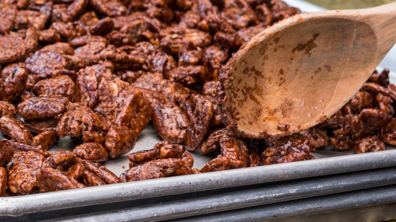 coated pecans on a sheet pan with wooden spoon