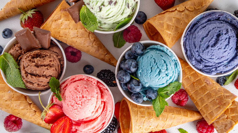 various ice cream flavors in bowls with fruit and cones scattered around