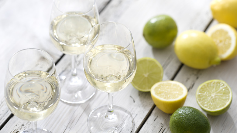 Three glasses of white wine with fresh lemons and limes