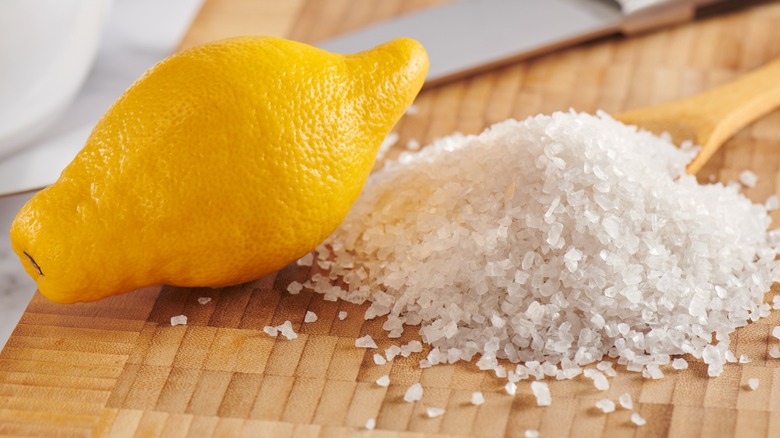 A whole lemon next to a pile of coarse salt on a wooden board