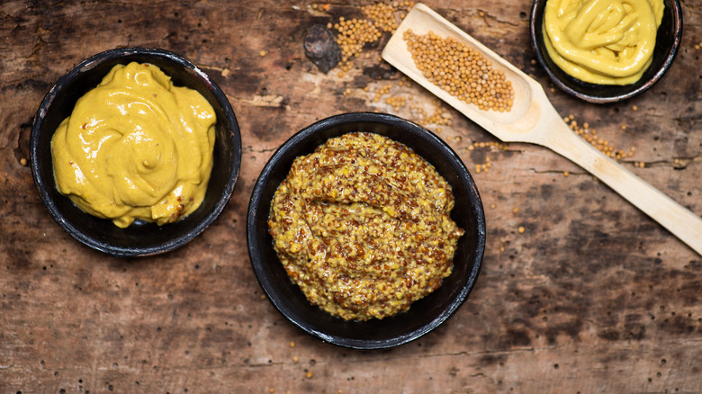 whole grain and dijon mustard in separate bowls on a wood table