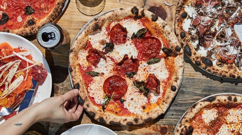 Hand reaching for salami pizza