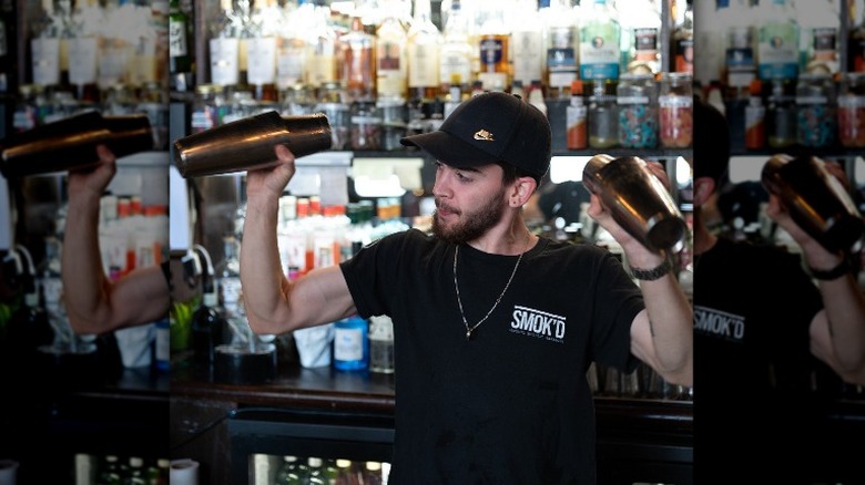 bartender in black shaking two cocktails