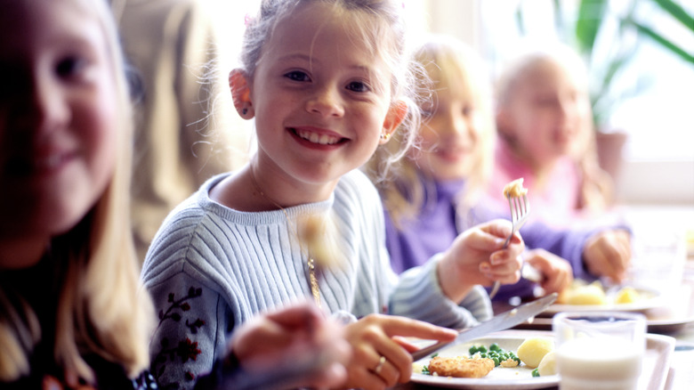 Kids smiling and eating lunch in a school cafeteria