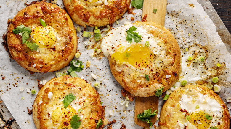 baked egg with cheddar, cilantro, and chives over a bagel on a parchment paper-lined baking sheet
