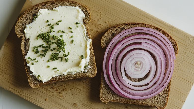 Open slices of wheat bread, one side with creamy spread and the other with red onion