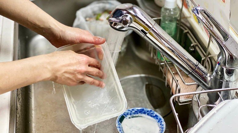 hands washing plastic container in sink