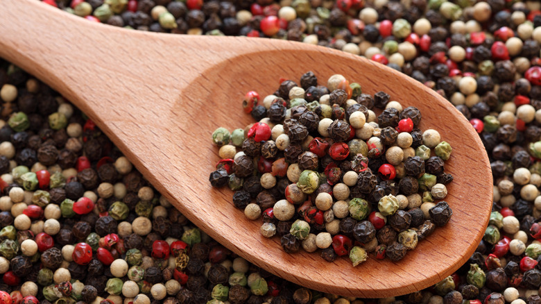 A wooden spoon filled with black, white, green, and pink peppercorns