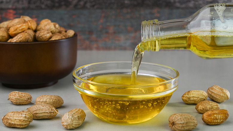 Peanut oil being poured into bowl surrounded by whole peanuts