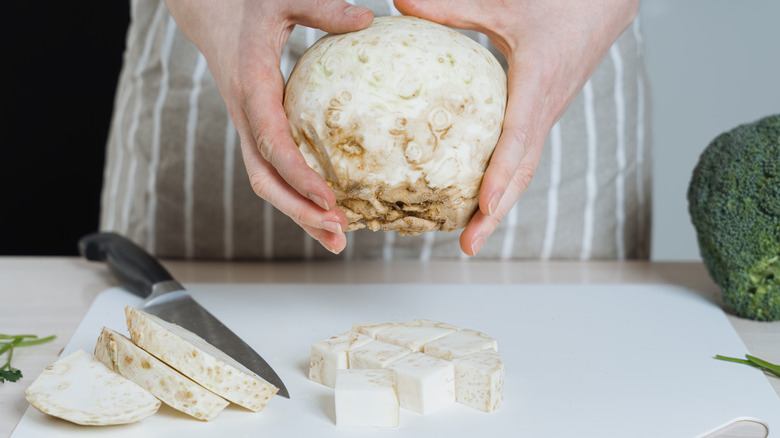 A chef holds a whole celeriac in their hands above plastic cutting board