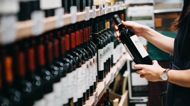 Hand grabbing bottle of wine off shelf