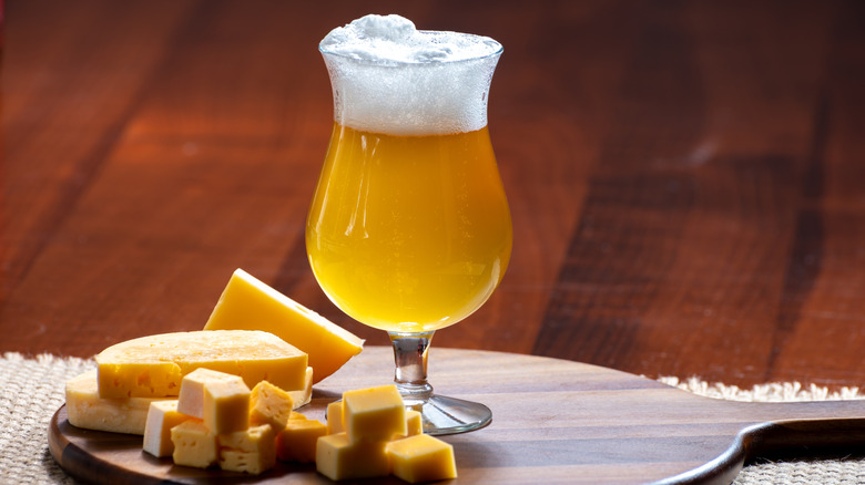 A foamy, golden beer in a Belgian-style glass along with a cheese board