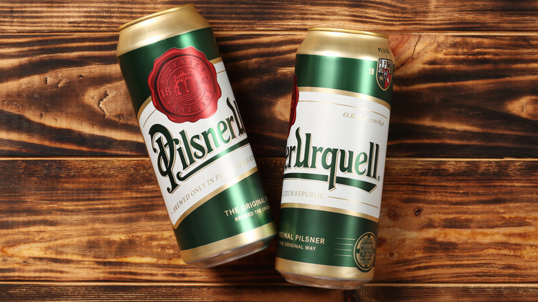 Two cans of Pilsner Urquell beer on a wooden background