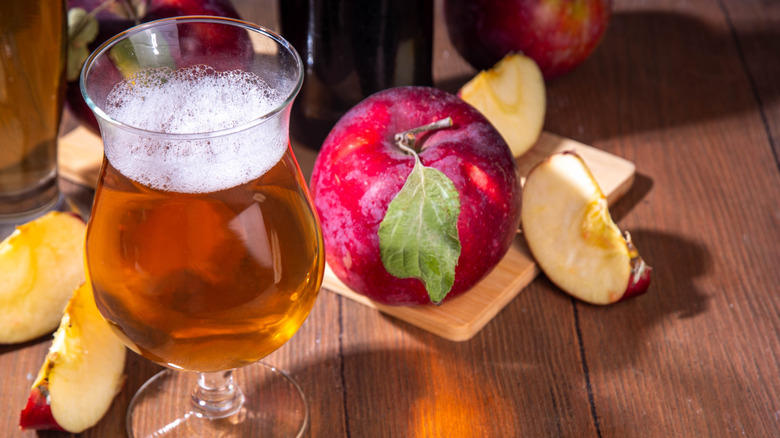 An amber colored ale in a Belgian style glass in front of fresh apples