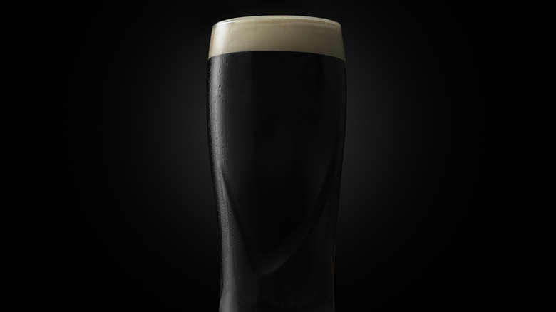 A dark-colored beer with creamy white foam against a black background