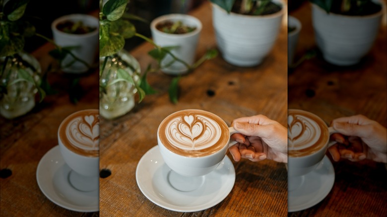 Person holding cup of coffee with latte art on top