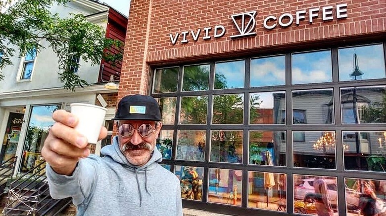 Man raising coffee cup in front of Vivid Coffee storefront