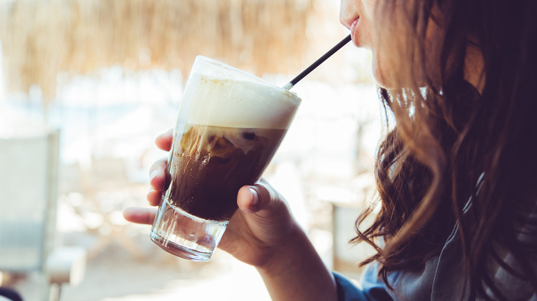 Person sipping an iced coffee with a thick layer of cold foam through a straw