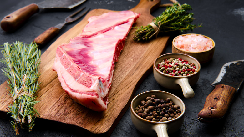 a raw lamb breast on cutting board with herbs and peppercorns