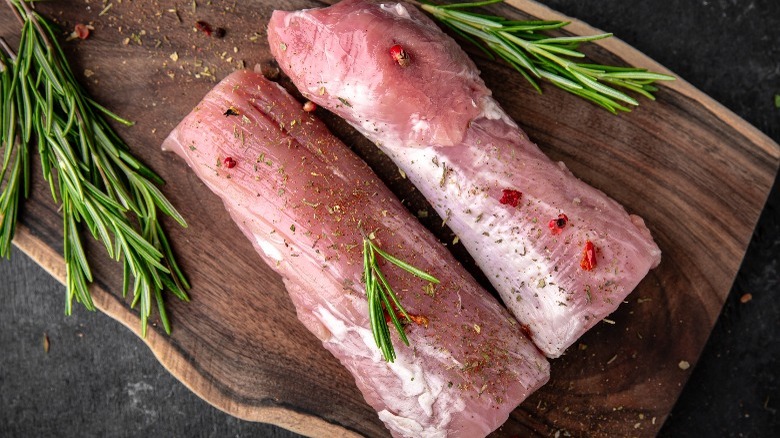 Two raw pork tenderloins with rosemary