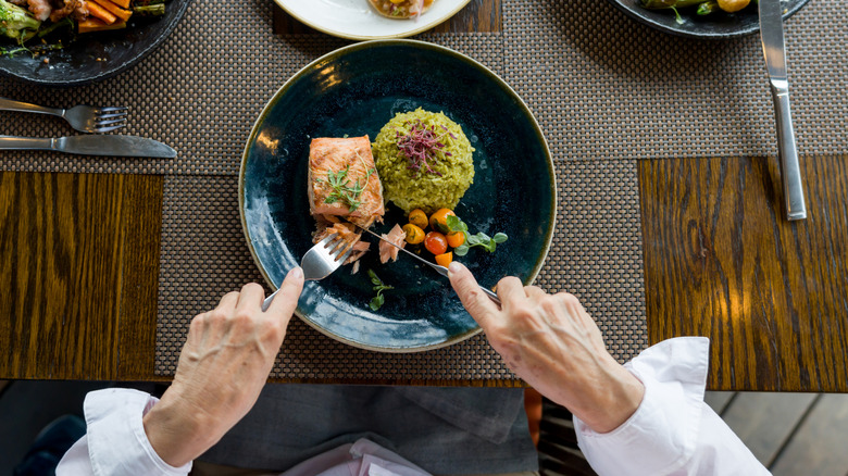 Aerial photo of a person cutting into a piece of salmon on a plate