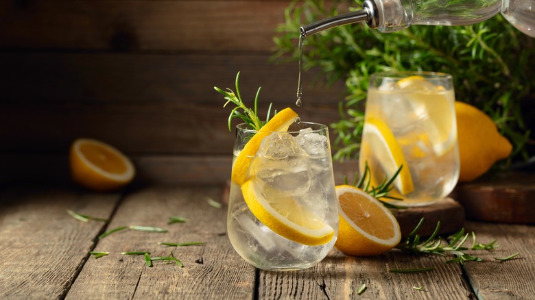 Gin and tonic with ice, lemon, and rosemary on a old wooden table