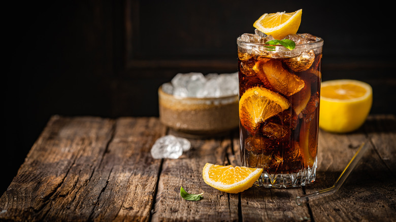 Cuba libre in a glass with brown rum, cola, mint, and lemon on wooden table