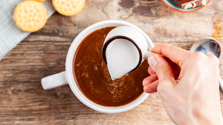 hand pouring creamer into coffee