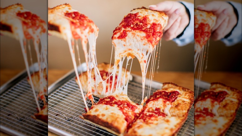 Person picking up a cheesy slice of Emmy Squared Pizza