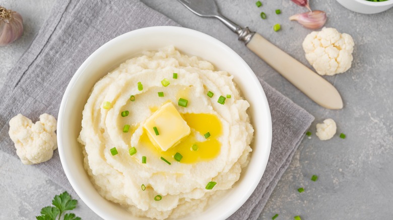 A bowl of creamy mashed cauliflower and parsley is shown