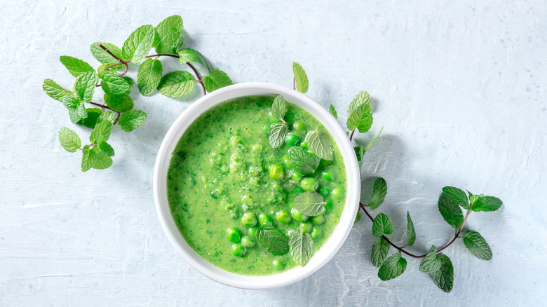 A bowl of mashed green peas with a sprig of mint around it.