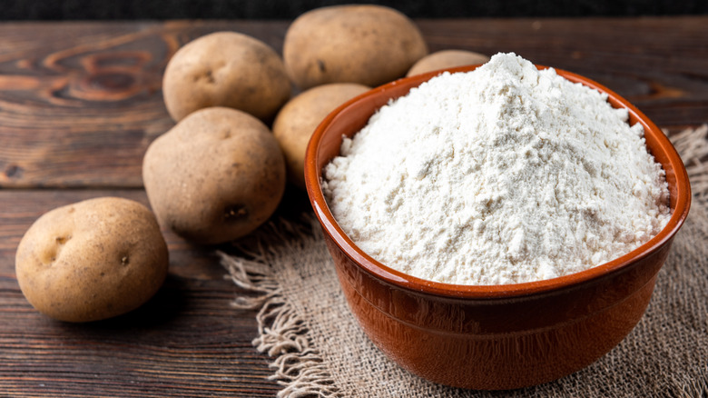 A bowl of potato starch alongside potatoes 