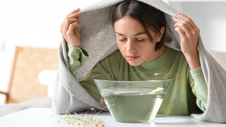 Woman inhaling steam from glass bowl