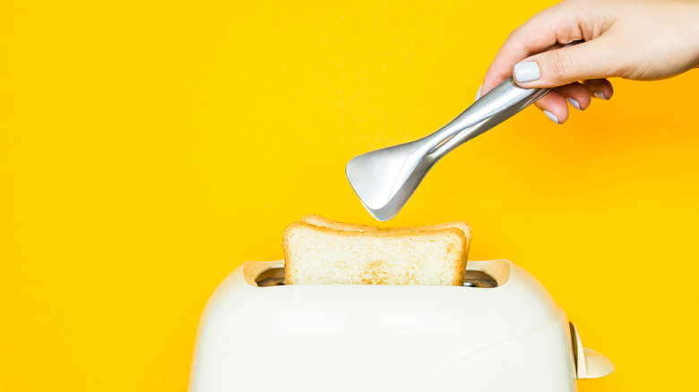 Tongs grabbing toast from toaster