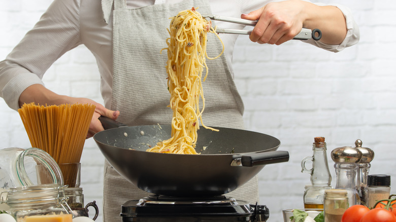 chef using tongs to toss spaghetti in wok