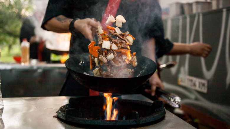 chef stir frying in wok over flame
