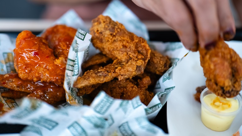 Hand dipping Wingstop chicken wings into sauce