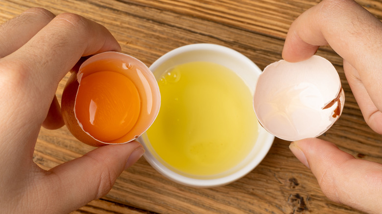 Hands separating an egg yolk from the egg whites