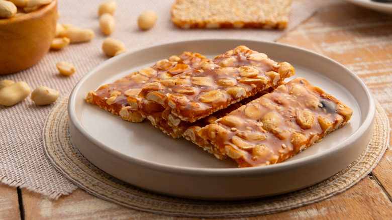 Small sheets of peanut brittle on a plate with a bowl of peanuts