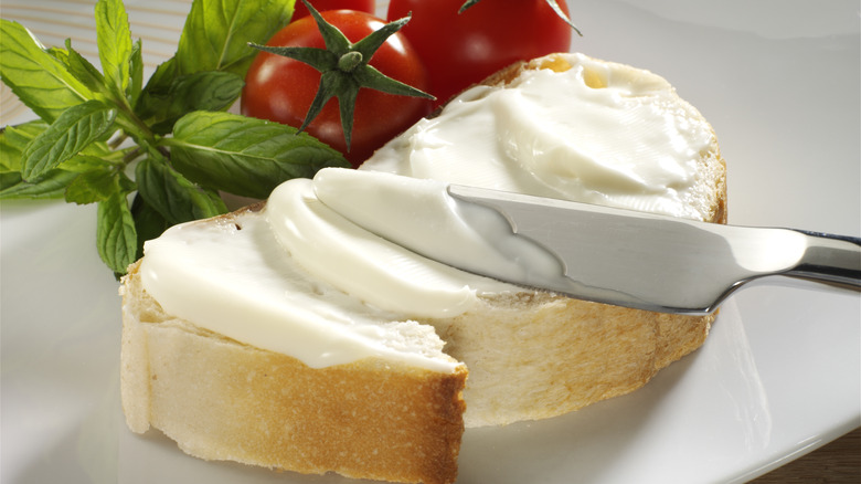 knife spreading cream cheese over slice of bread with tomato and basil