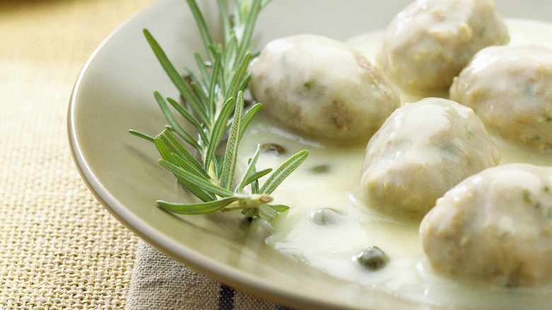 Close up of breaded cutlets in a cream sauce with rosemary sprig