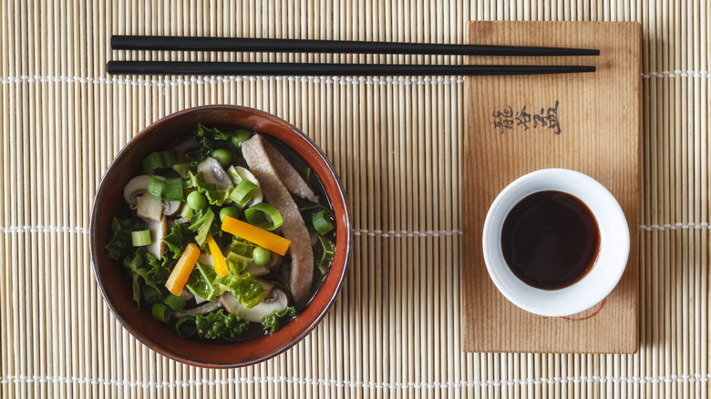 Bowl of Asian food and chopsticks with small bowl of soy sauce on the side