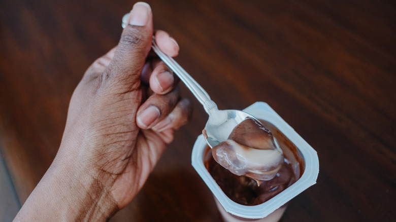 Hand eating from a pudding cup with a metal spoon