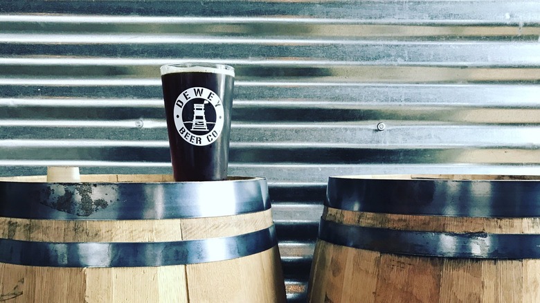 Dewey Beer glass sitting on top of wooden barrel containing beer