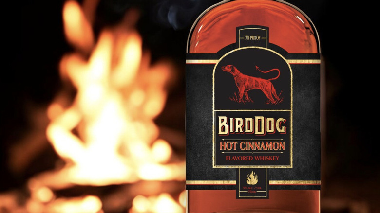 A bottle of Bird Dog Hot Cinnamon whiskey by a fire