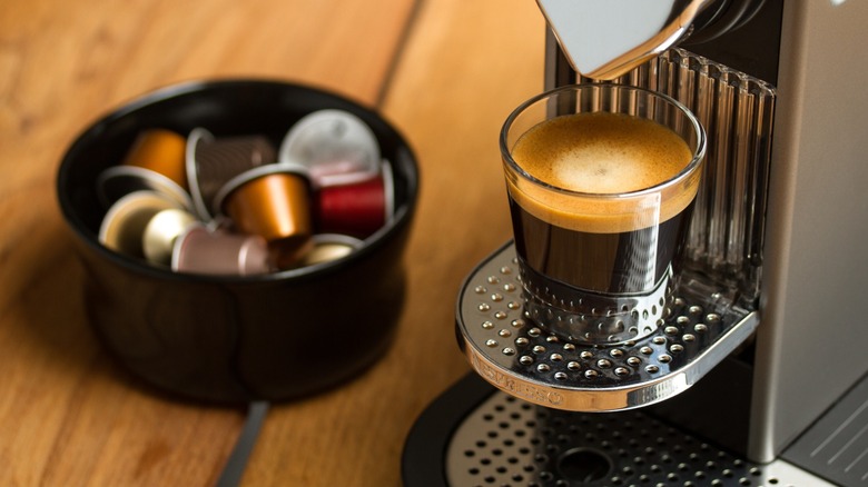 Espresso shot on machine next to coffee pods