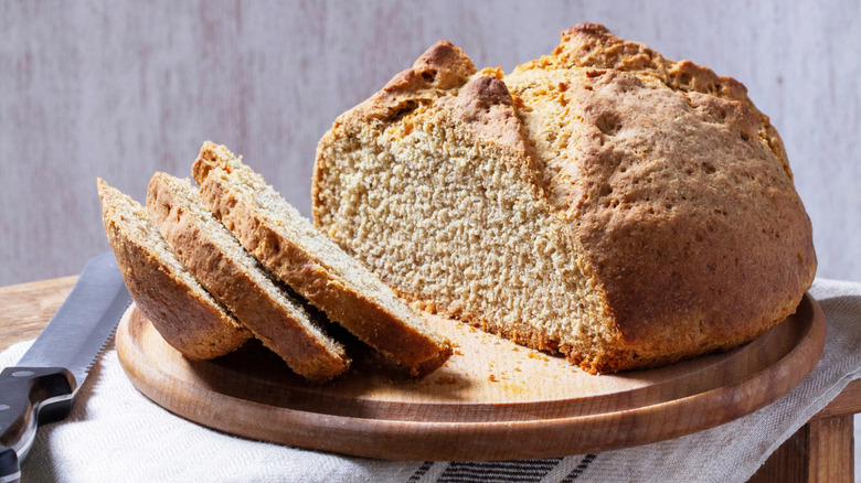 A loaf of Irish soda bread on a wooden board next to bread knife