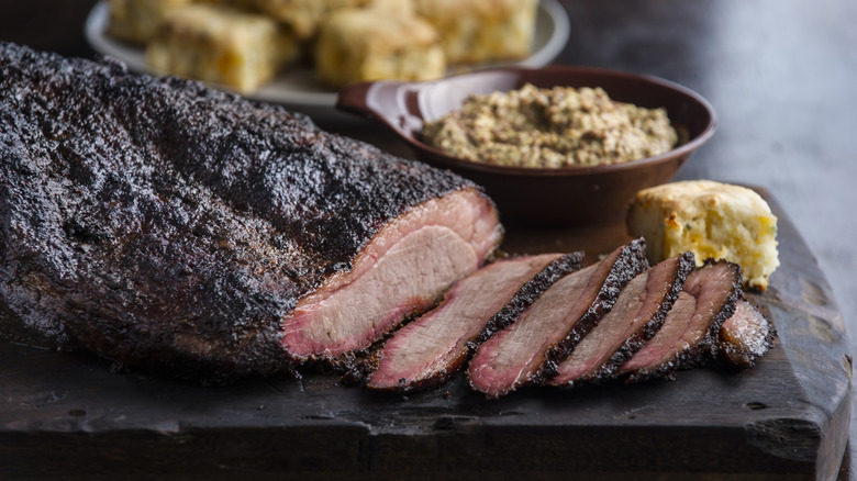 Sliced brisket on a cutting board beside a cornbread roll